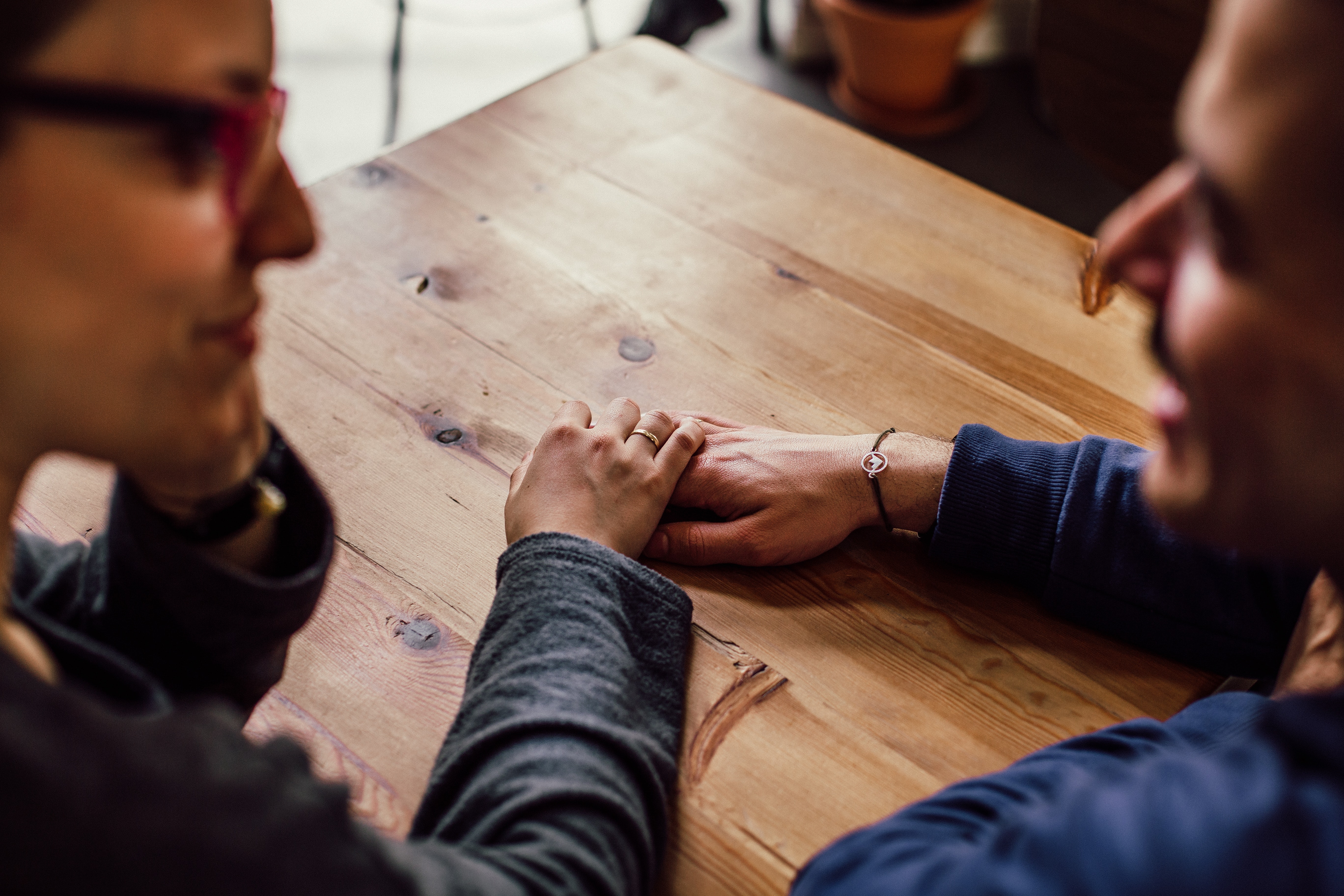 Man and woman talking and holding hands on a wooden table. 