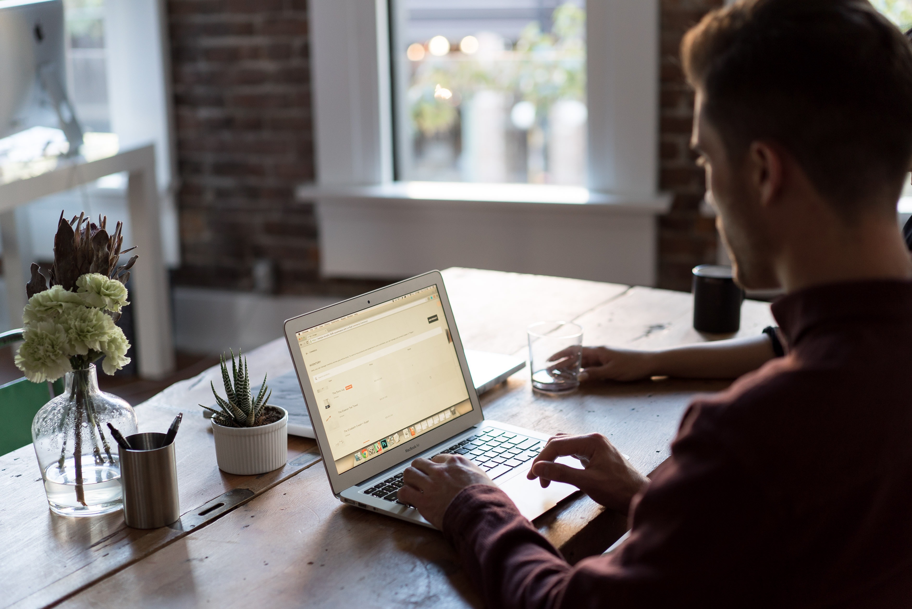 Man in a red shirt typing on a laptop on a wooden table